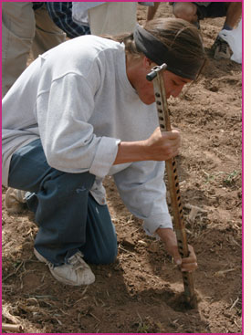A Pueblo farmer using a metal digging stick to plant seed.